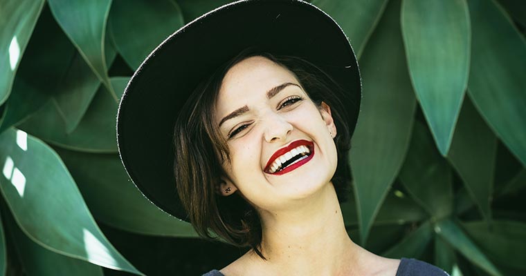 Young woman wearing red lipstick and black hat smiling.
