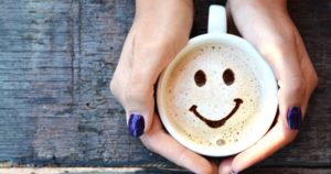 female holding a cup of coffee with smiley face, and coffee can lower cancer risk.